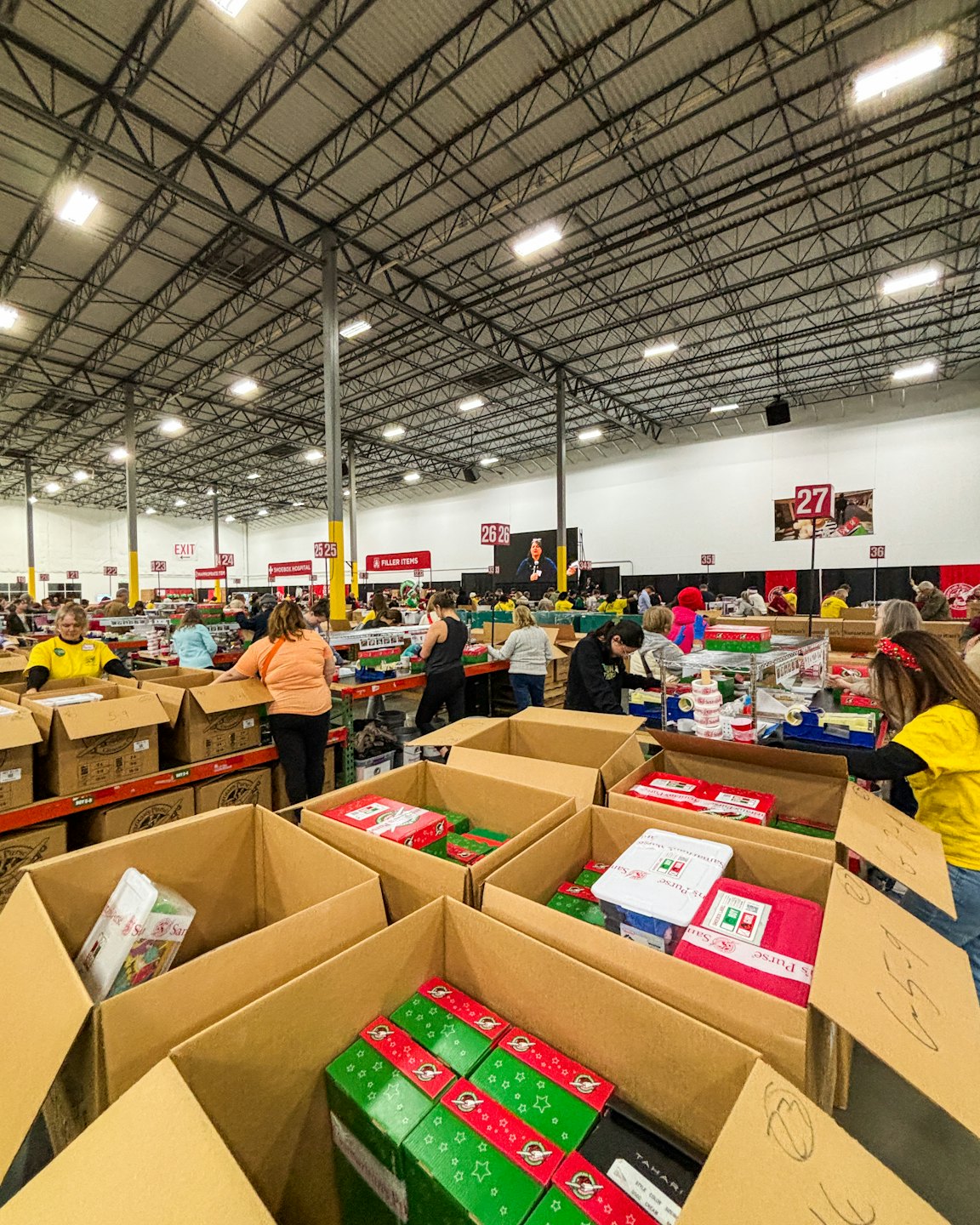 Diverse volunteers pack holiday gifts into boxes in a warehouse.