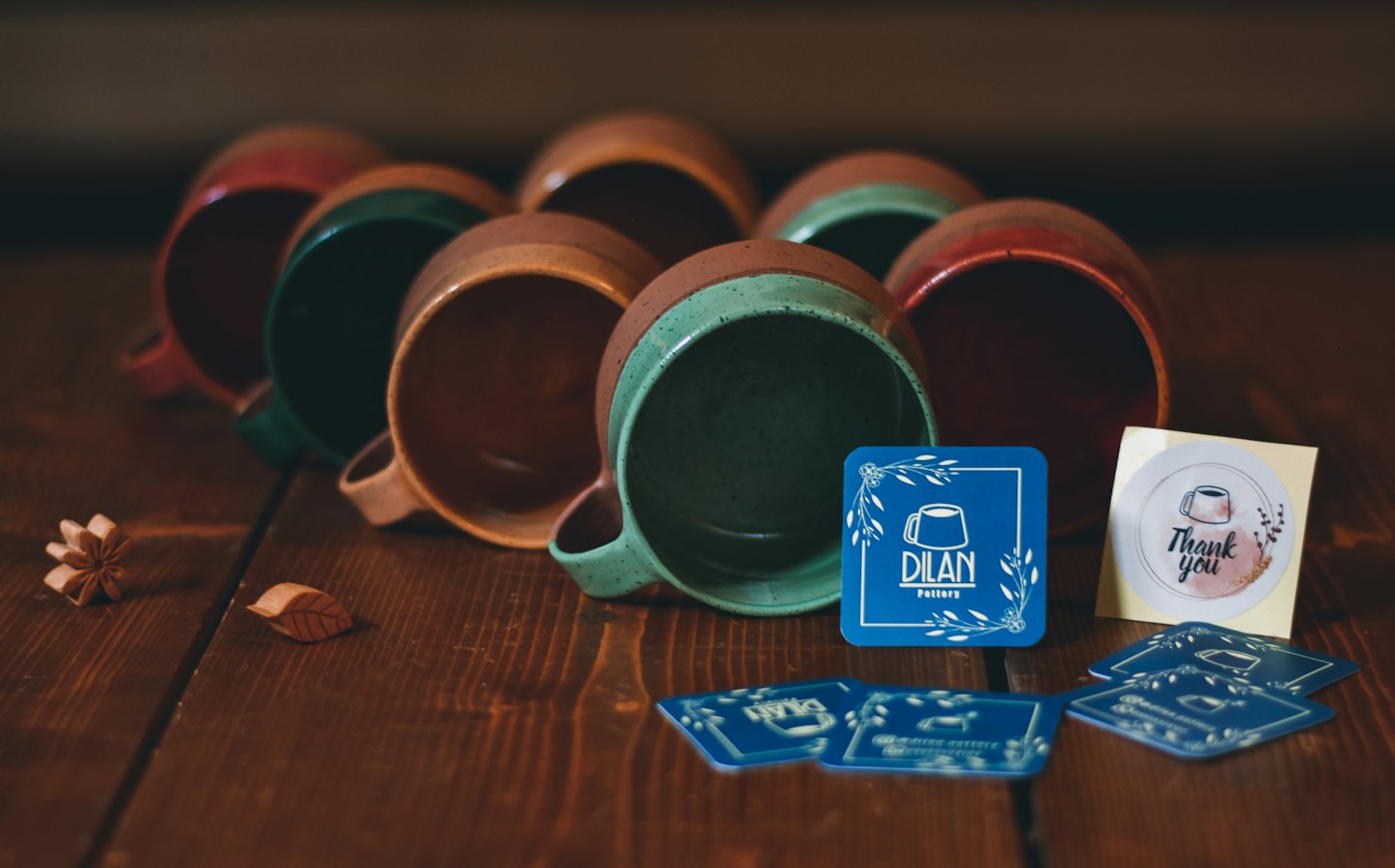 Ceramic mugs and branded pottery cards sit on a wooden surface.