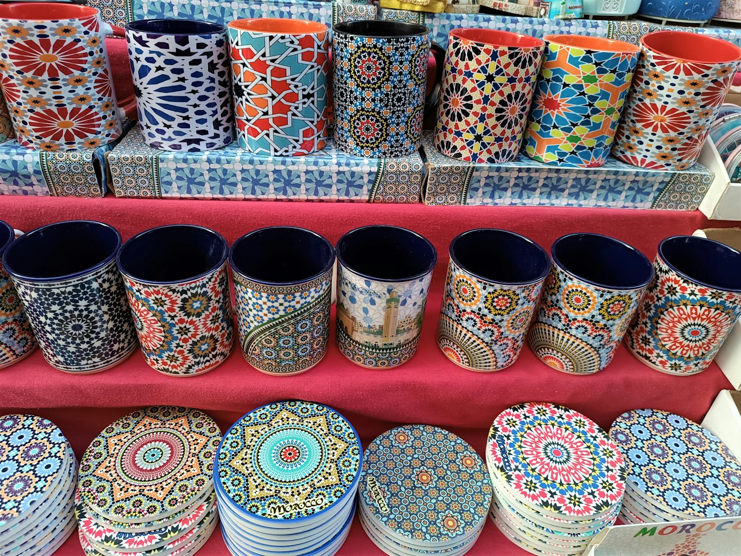 Colorful ceramic mugs and coasters with geometric patterns on pink shelves.